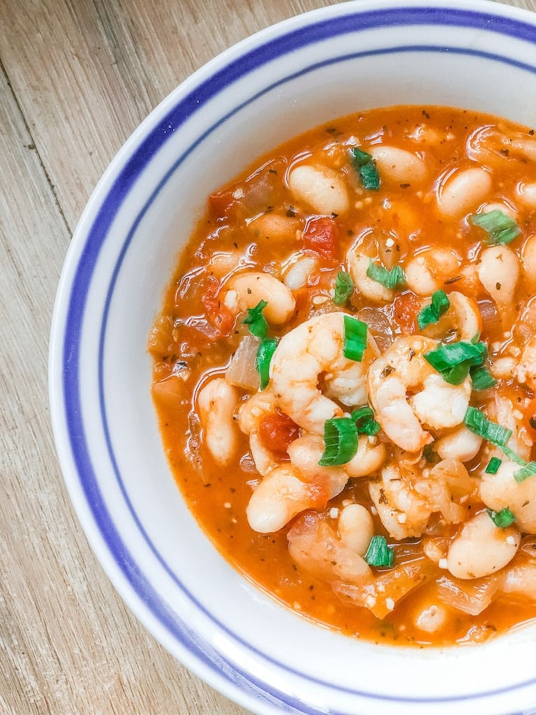 white bean and shrimp soup in a white ball on a wooden table